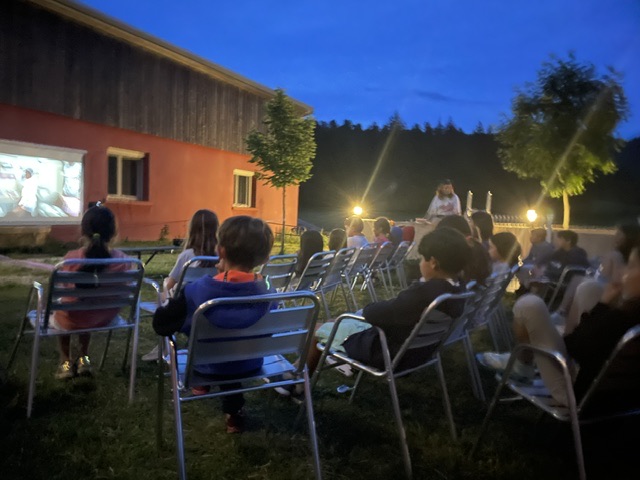 Open-air cinema screening at dusk, projected onto the lodge wall